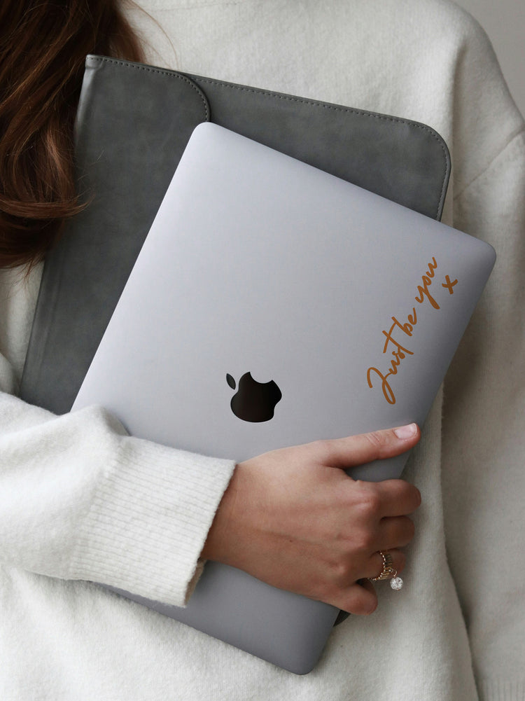 Person holding a gray laptop with a sticker and text