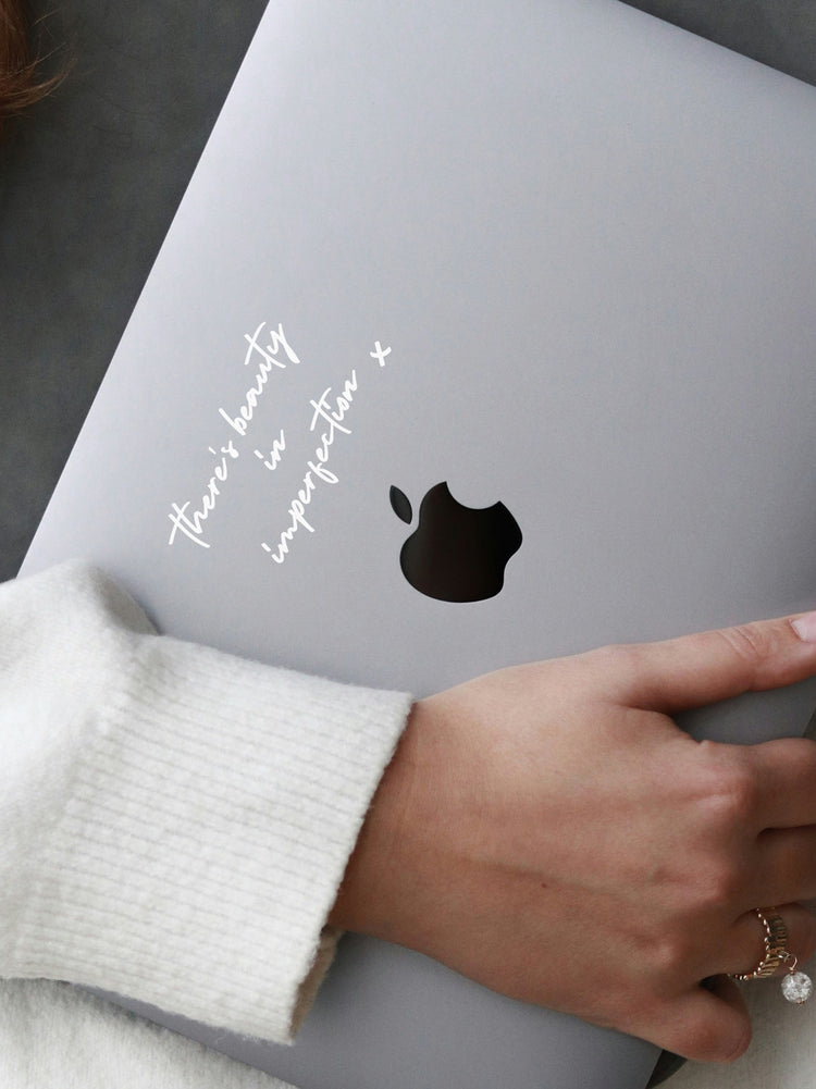 Person holding a laptop with a black decal and white text on a gray surface