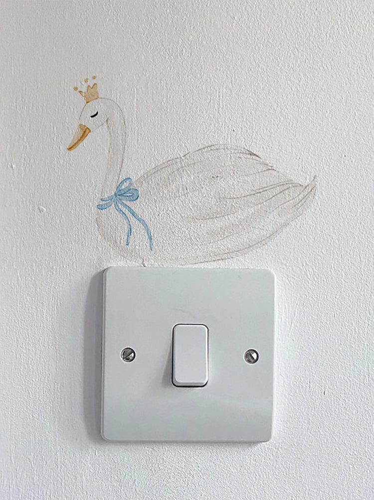 Decorative swan sticker with a crown and blue bow on a light switch.