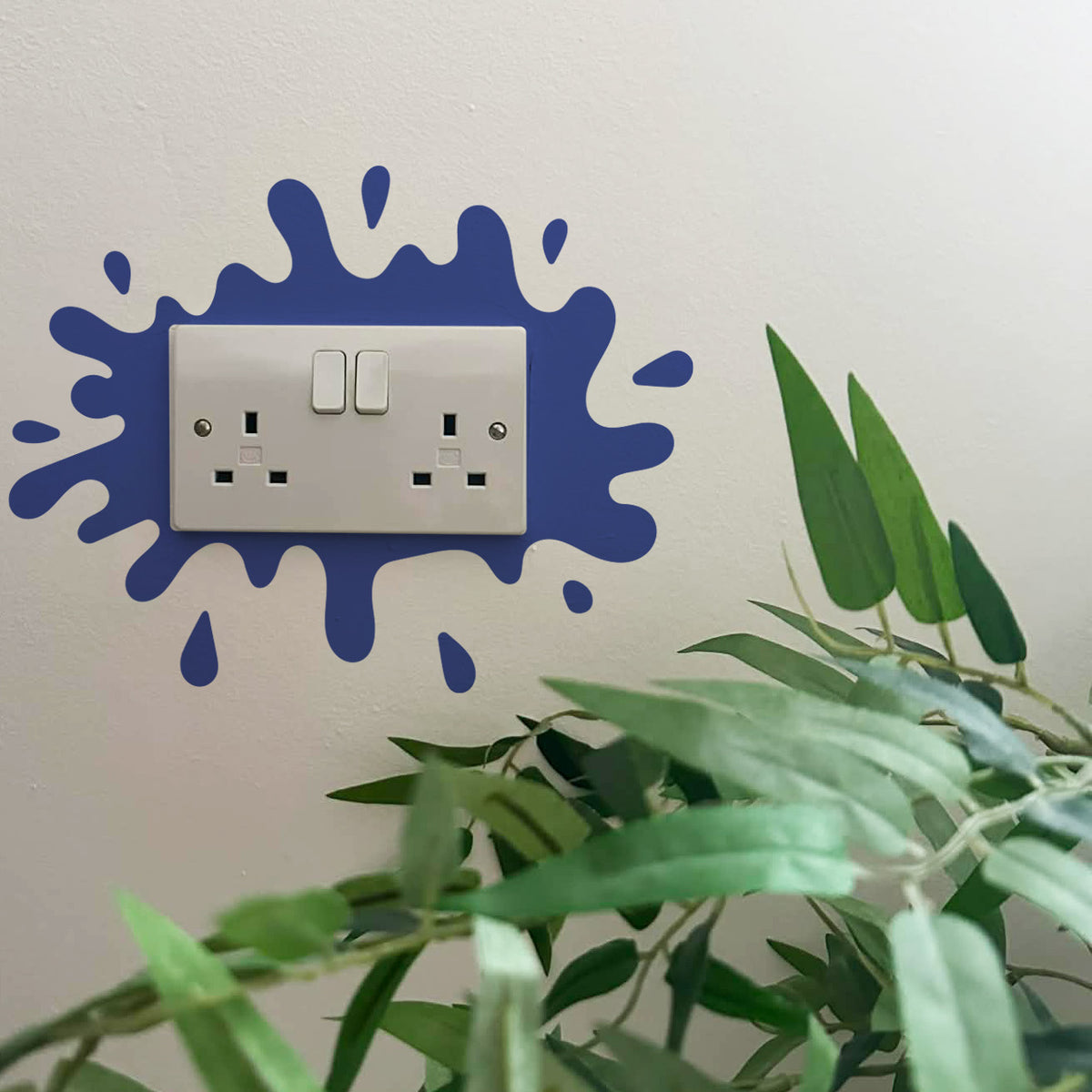 Decorative Paint Splat Plug Socket in Navy, surrounded by green leaves.