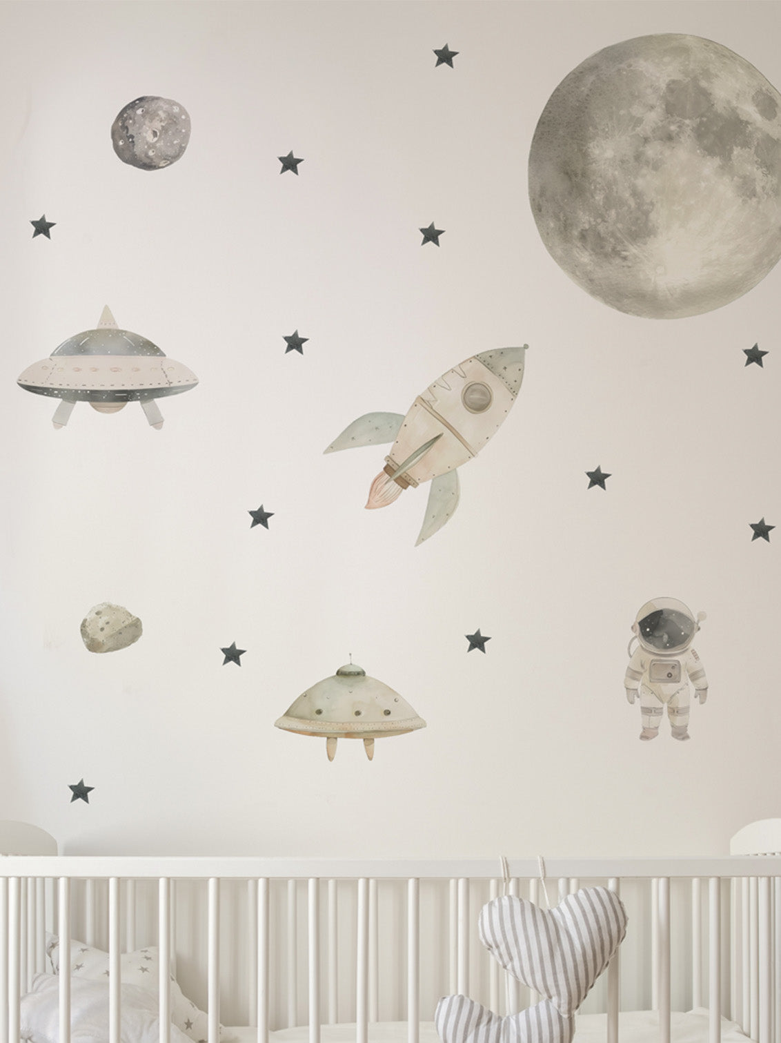 Space-themed wall decals including a rocket, UFOs, and an astronaut on a light gray wall above a crib.