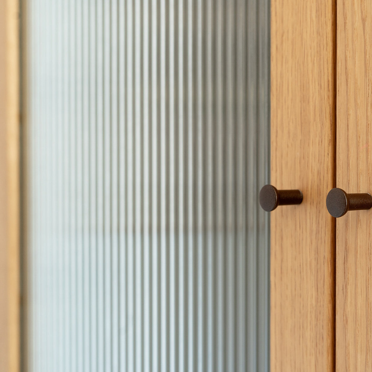Wooden cabinet with glass door covered in a reeded window film featuring two round handles.