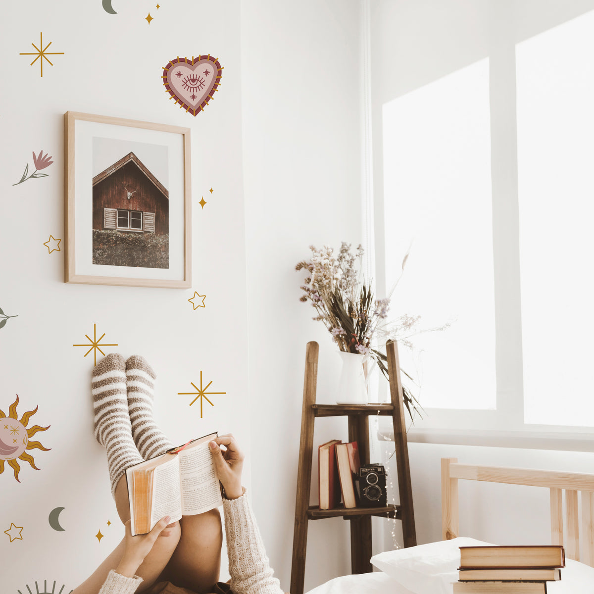 Person reading a book in a cozy room with a ladder, books, and decorative wall art.