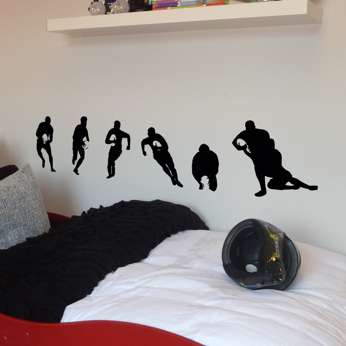 Set of 6 Rugby player silhouttes in black under a shelf and above a bed with a grey cushion and black throw