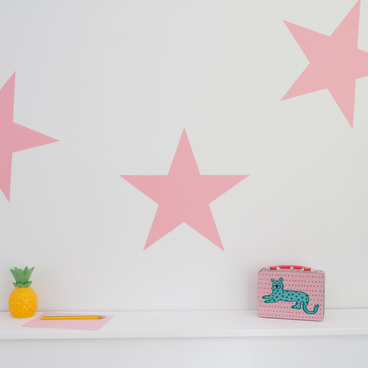 A set of large, pink colored stars wall stickers displayed on a wall, with a cat-shaped storage box and a pineapple decoration on a white surface.