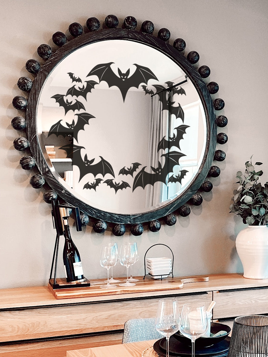 Round mirror with bat wreath wall sticker decoration on a wall above a side board.