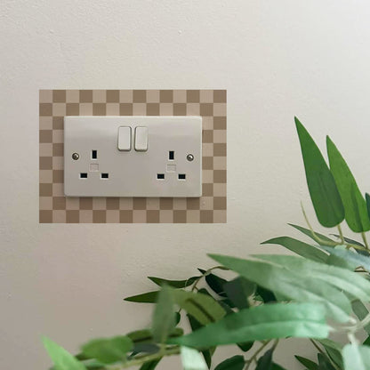 Decorative wall sticker with a Brown &amp; cream checkered border over a light switch on a wall with a plant in the foreground.