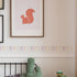 white wall with a picture frames below that is a candy stripe sticker above a dado rail, black bedframe with a green cusion