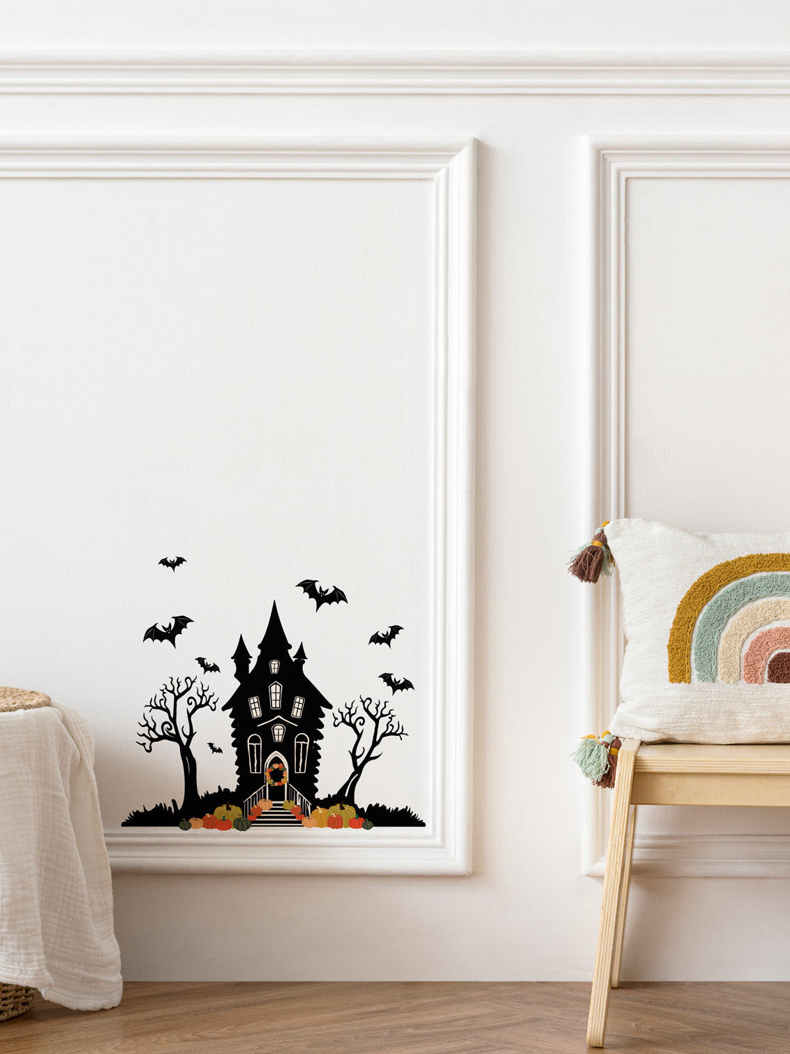 Framed Halloween-themed wall art with a haunted house and bats in a room with a chair and decorative pillow.
