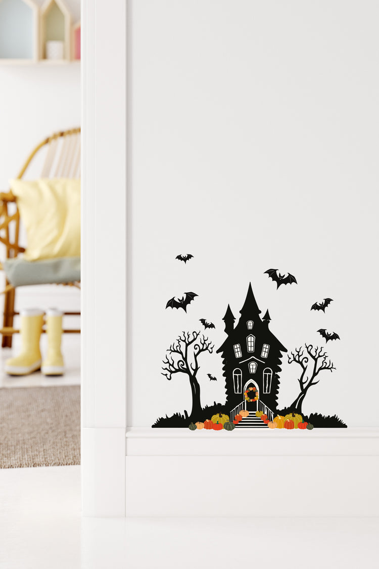 Halloween-themed wall decal of a haunted house with bats and pumpkins on a white wall.