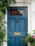 Blue door with decorative elements and plants on a white wall