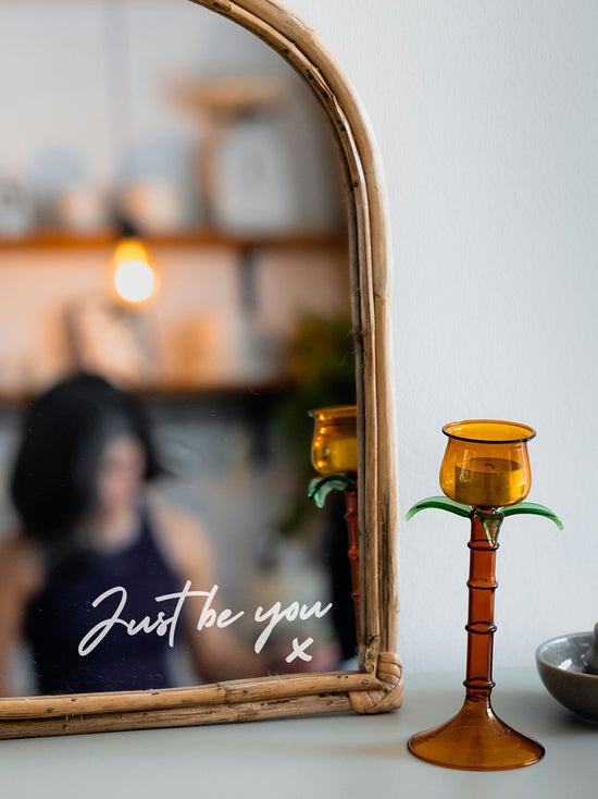 Amber candle holder on a surface with a mirror reflecting a blurred indoor setting.