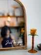 Amber candle holder on a surface with a mirror reflecting a blurred indoor setting.
