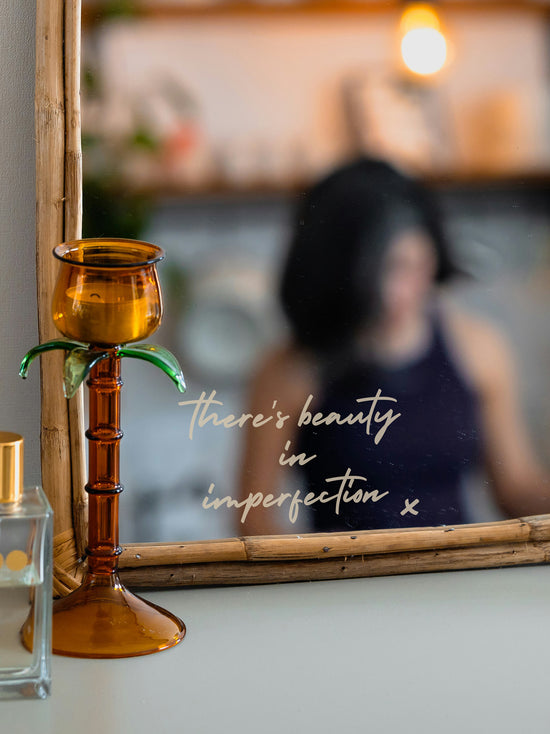 Decorative mirror with palm tree candle holder and blurred person in the background