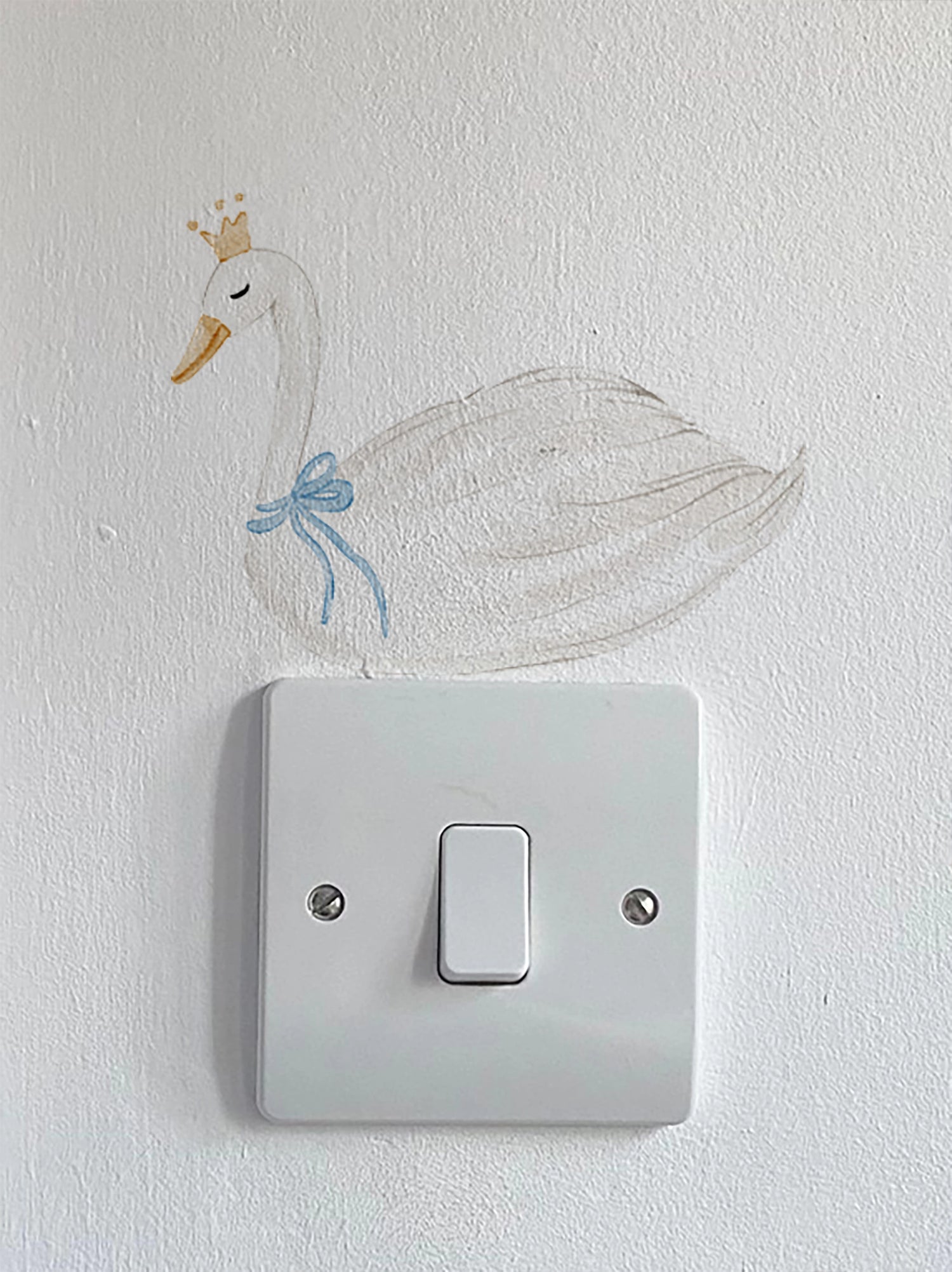 Decorative swan sticker with a crown and blue bow on a light switch.