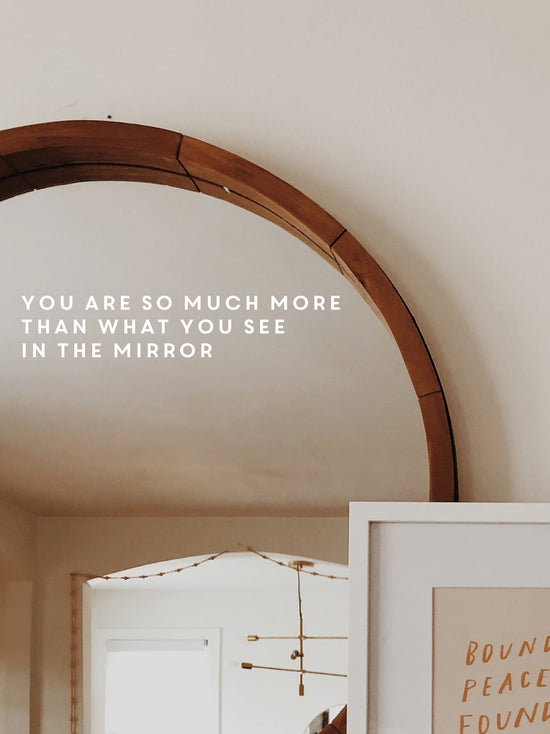 Round wooden mirror with motivational quote on a neutral wall.