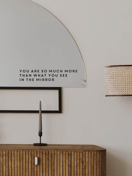 Decorative mirror with motivational quote above a wooden cabinet.