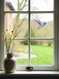 A vinyl hummingbird wall sticker and window decal applied to a window pane, with a vase of flowers on the windowsill and a view of a garden outside.