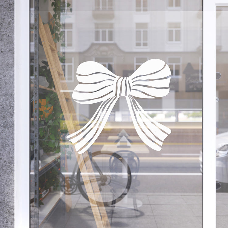 Decorative white bow design on a glass door with a blurred street scene in the background.