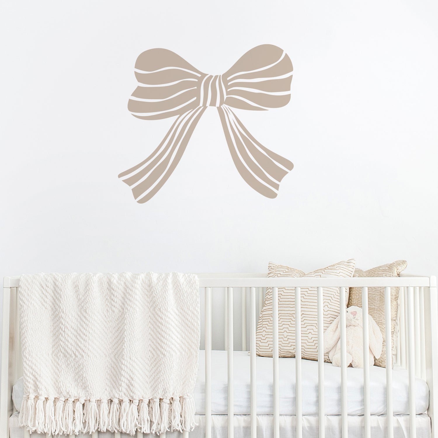 Mushroom coloured bow wall decal above a crib with white bedding and decorative pillows.