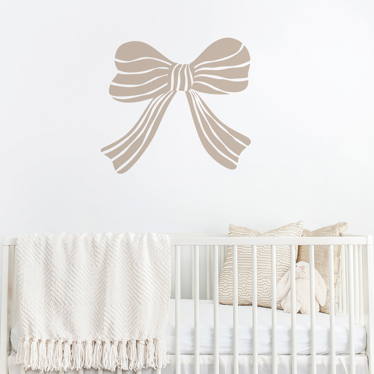 Mushroom coloured bow wall decal above a crib with white bedding and decorative pillows.