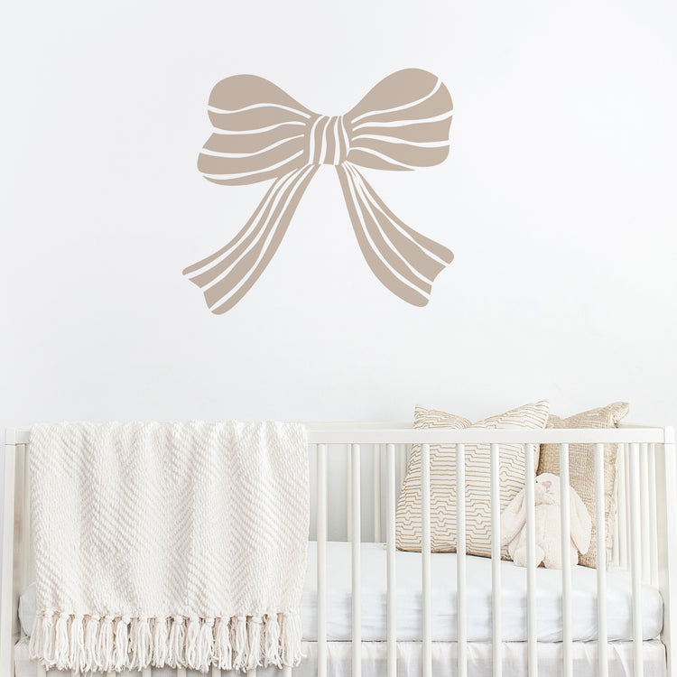 Mushroom coloured bow wall decal above a crib with white bedding and decorative pillows.