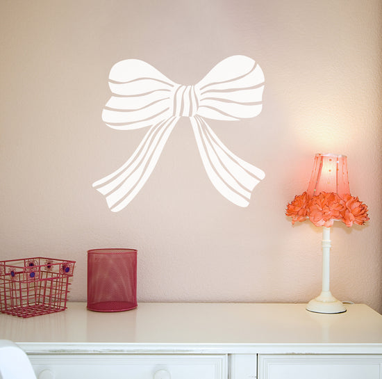 Wall decal of a large white bow on a light pink wall with a small table and lamp in the foreground.