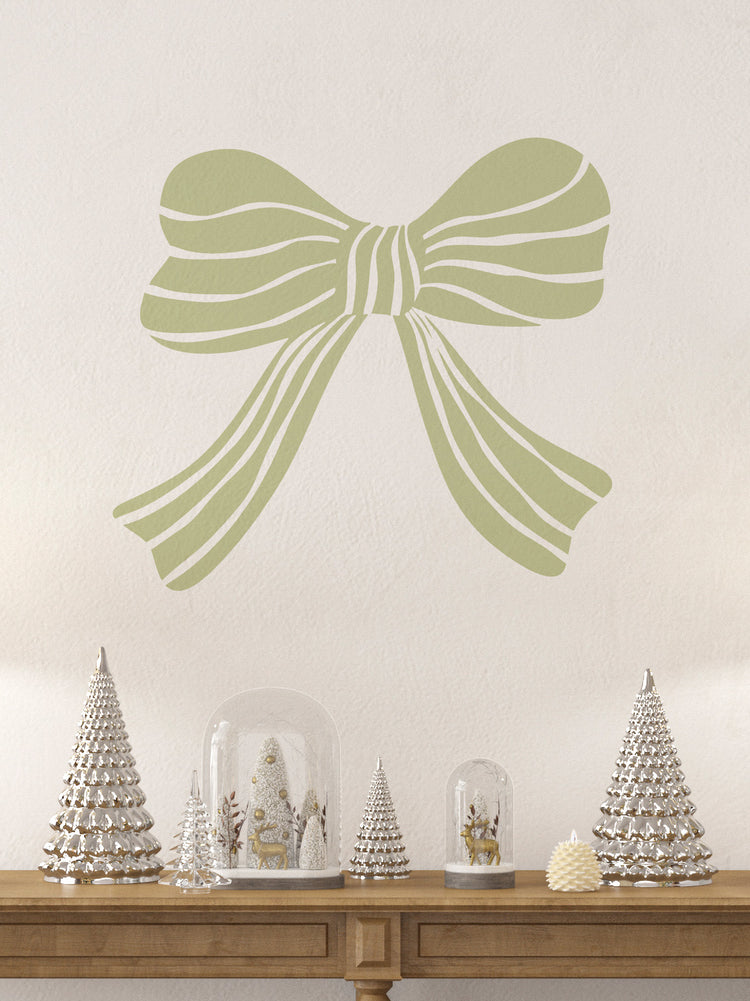 Decorative willow green bow wall decal with Christmas trees and snow globes on a wooden table.