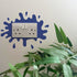 Decorative Paint Splat Plug Socket in Navy, surrounded by green leaves.