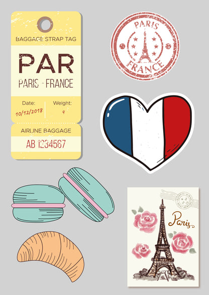 Collection of Paris-themed items including a luggage tag, heart-shaped sticker with French flag, macarons, and Eiffel Tower postcard on a gray background.