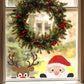 A festive Christmas window decoration featuring a brown reindeer head sticker with large antlers, a red nose, and white eyes, next to a santa head sticker with a red hat, white beard, black gloves and a cheeky face, positioned below a green pine garland with red berries.