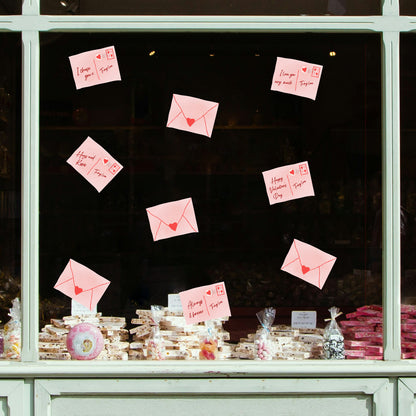 Love letters with heart symbols attached to a window display with baked goods below.