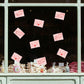 Love letters with heart symbols attached to a window display with baked goods below.