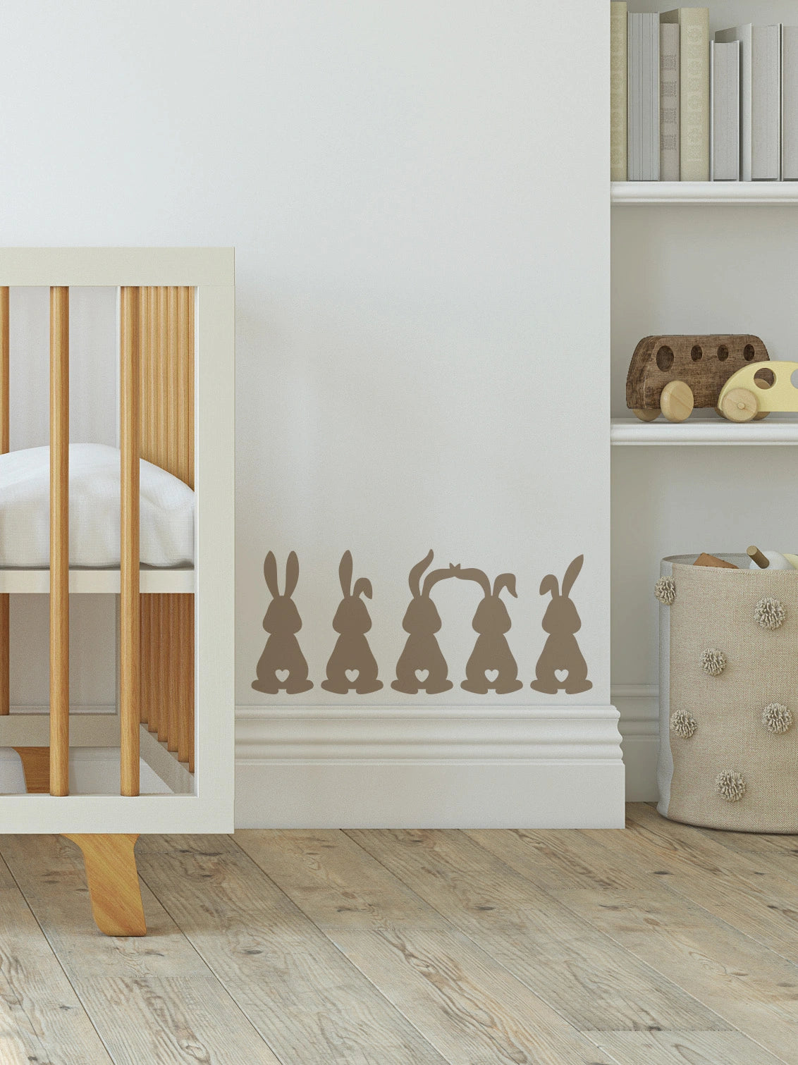 white wall with five bunny stickers, with a white and wooden cot next to it and shelves with books and wooden toys on it.