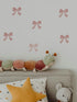 Decorative wall stickers of pink bows on a light gray wall above a sofa with plush toys.