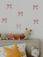 Decorative wall stickers of pink bows on a light gray wall above a sofa with plush toys.
