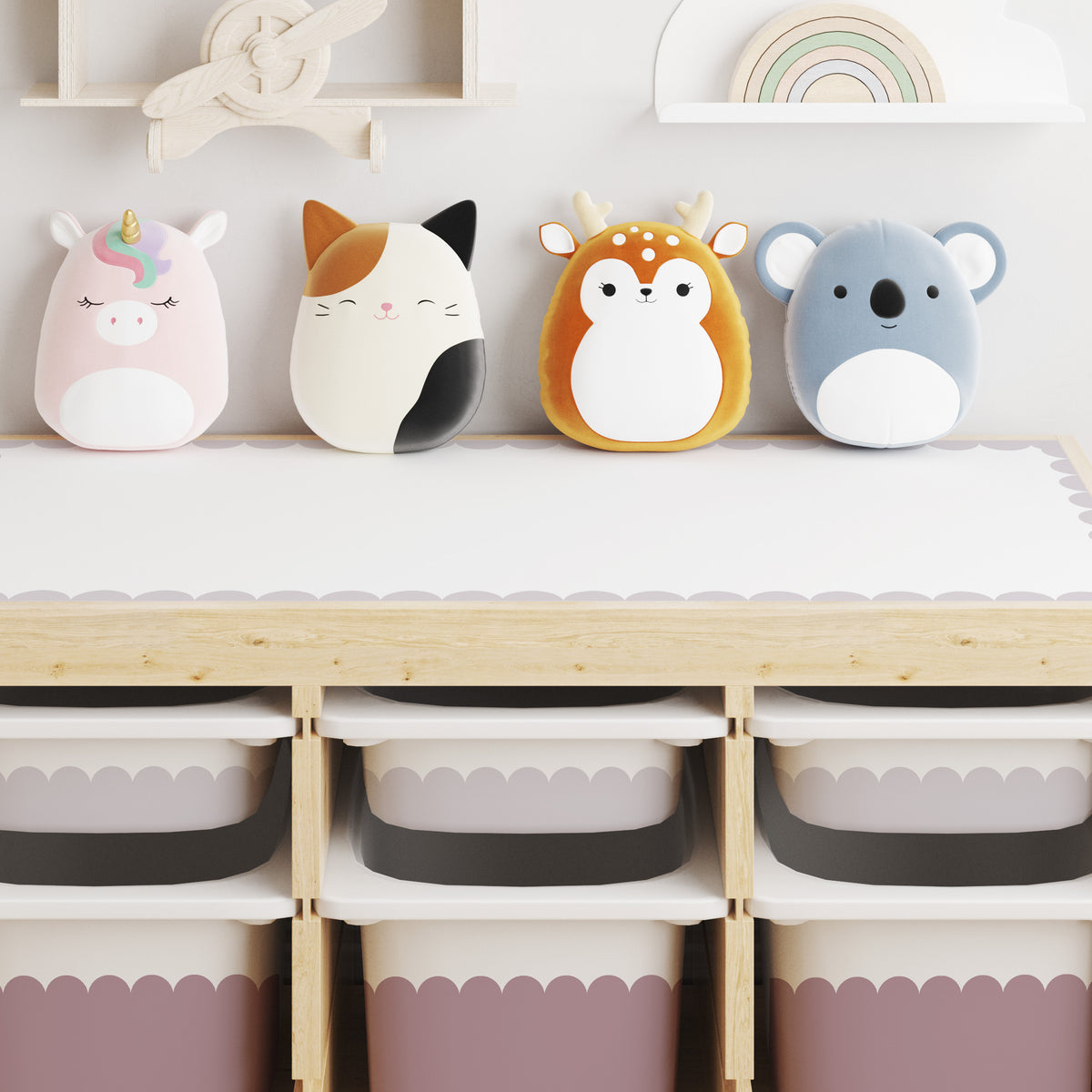 Four plush animal storage bins shaped like a unicorn, cat, deer, and koala, lined up on a light wood trofast storage unit with small drawers in Dusky Lilac and large drawers in Rose Dusk.