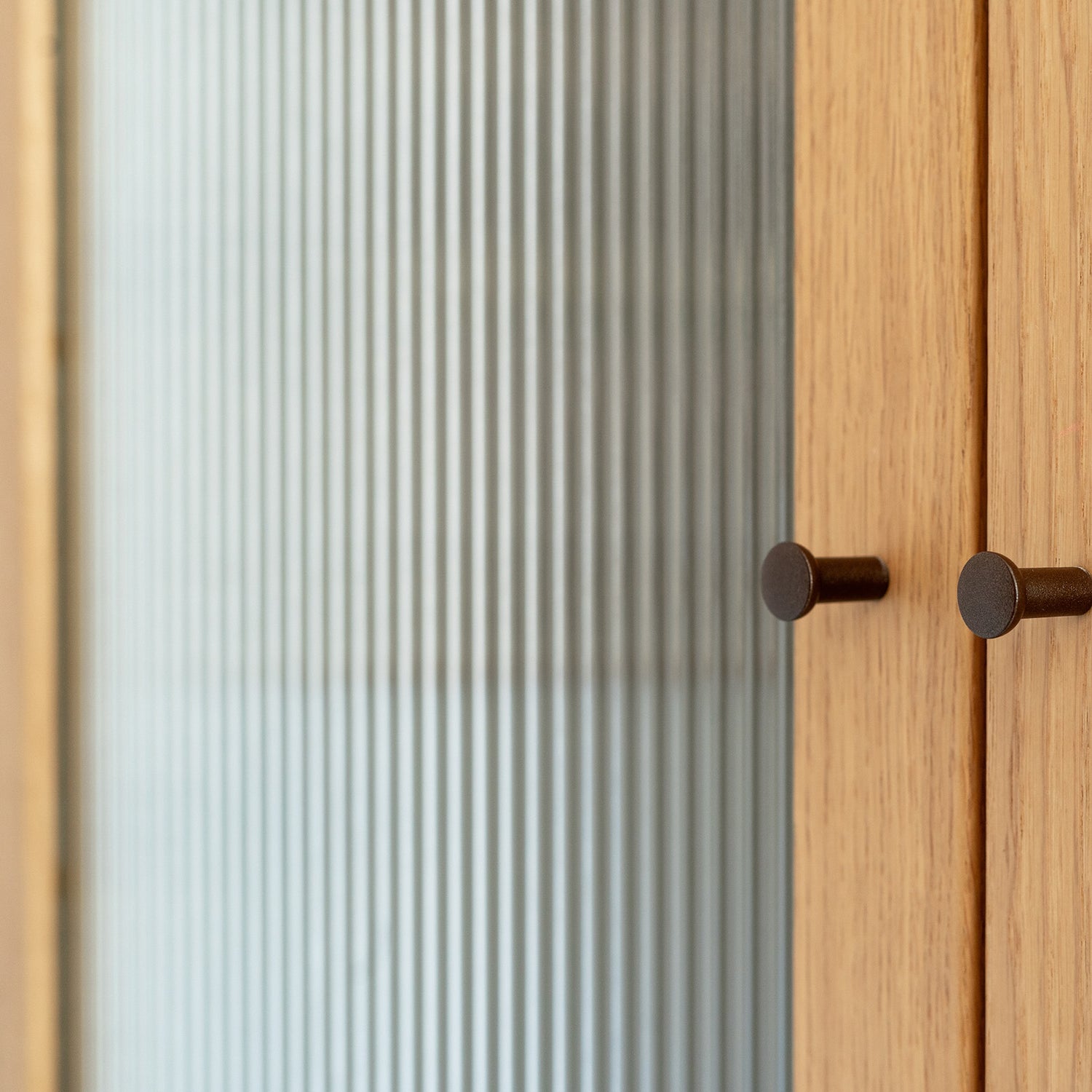 Wooden cabinet with glass door covered in a reeded window film featuring two round handles.
