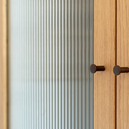 Wooden cabinet with glass door covered in a reeded window film featuring two round handles.
