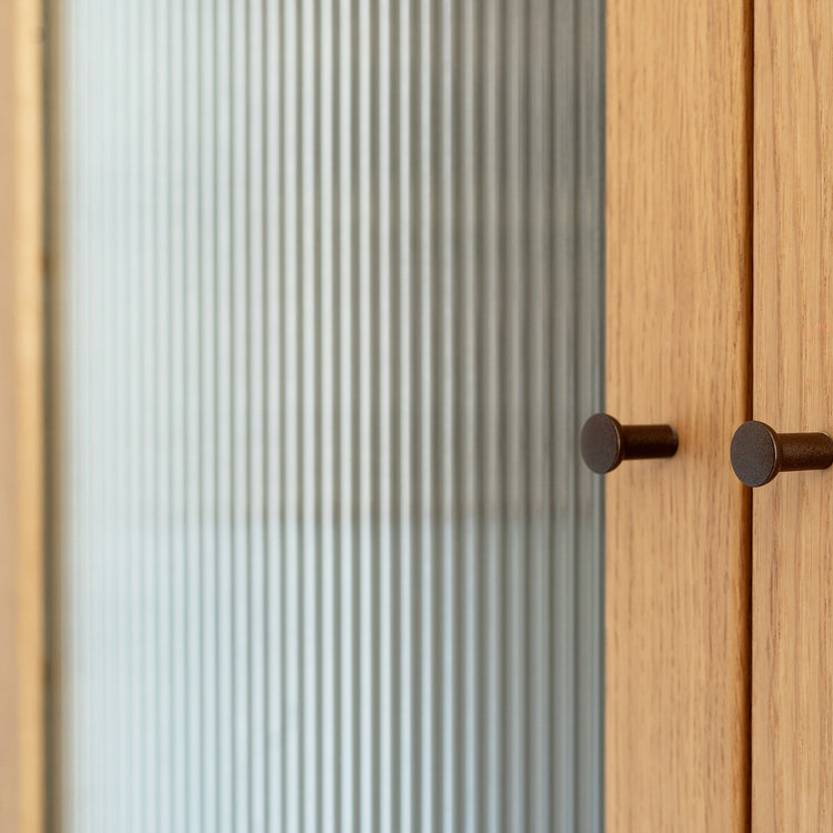 Wooden cabinet with glass door covered in a reeded window film featuring two round handles.
