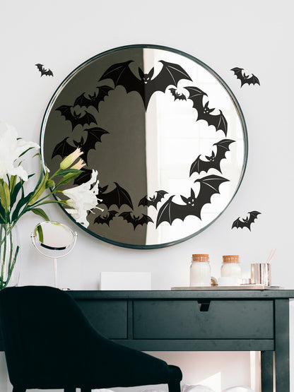 Round mirror with black bat decals on a white wall above a dark wooden desk.