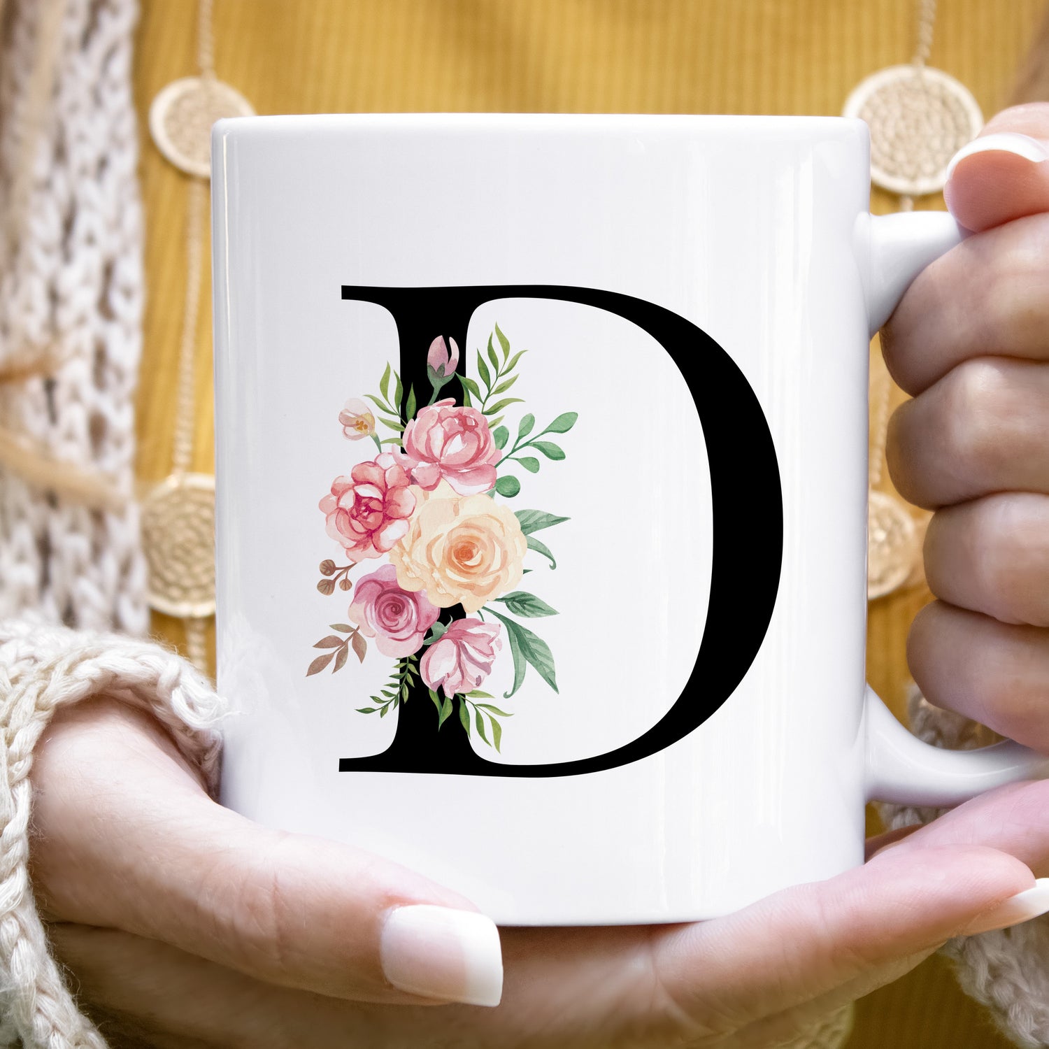 Person holding a white mug with a floral letter &