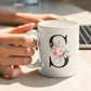 Person holding a white mug with floral letter &
