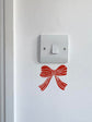 Light switch with a red bow design on a white wall