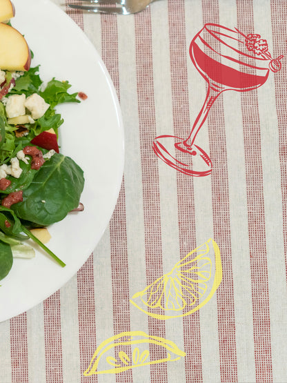 Placemat with red wine glass and lemon design on a striped tablecloth, next to a plate of salad.