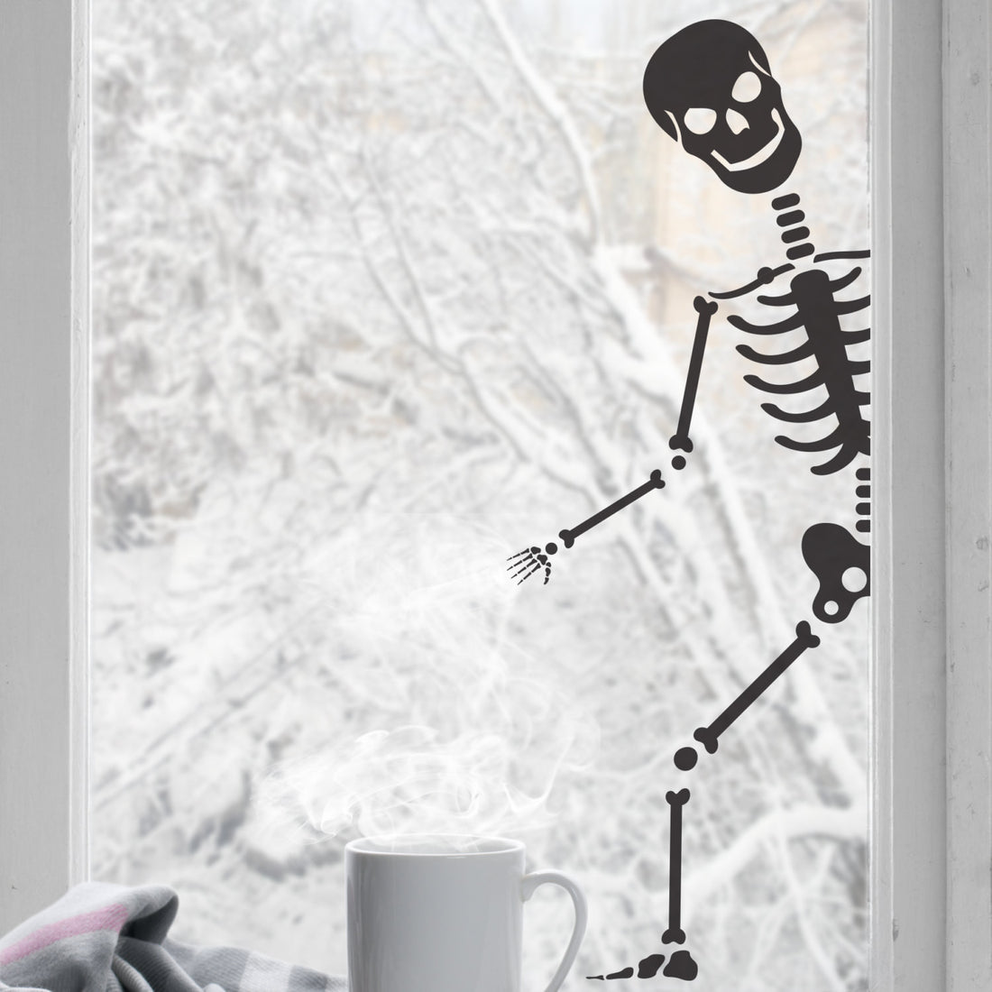 A black colored peeping skeleton sticker shown peeping through a window, with a cup of coffee and a blanket in the foreground.