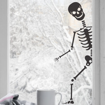 A black colored peeping skeleton sticker shown peeping through a window, with a cup of coffee and a blanket in the foreground.