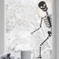 A black colored peeping skeleton sticker shown peeping through a window, with a cup of coffee and a blanket in the foreground.