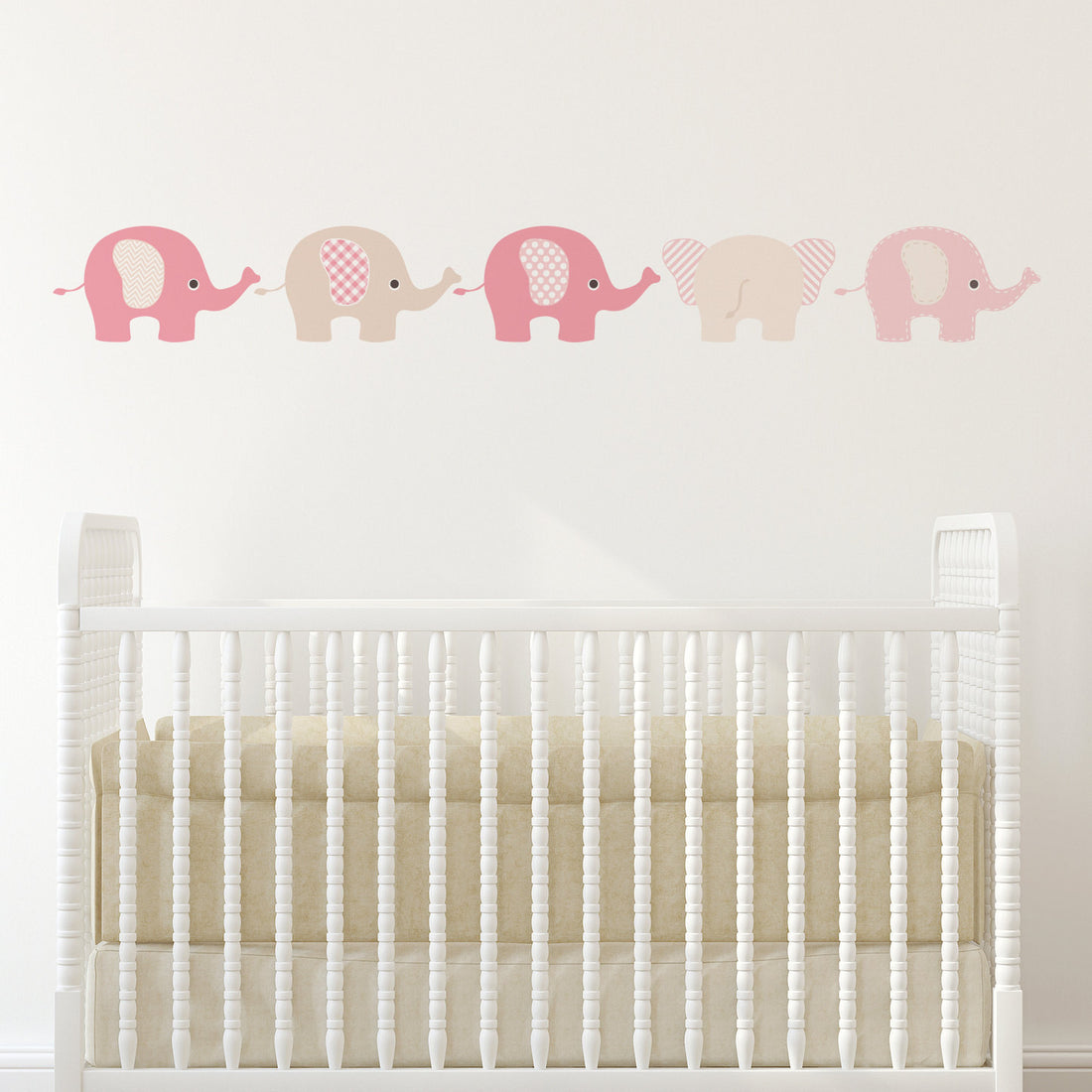 A set of five pink elephant nursery wall stickers of varying sizes placed on a white wicker baby crib.